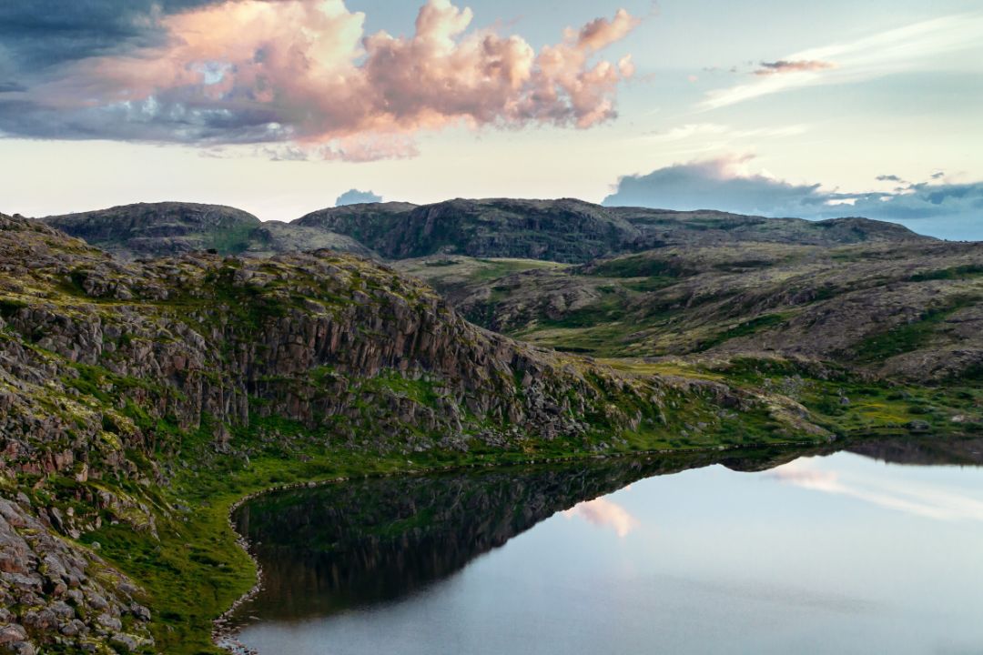 Photo of a bay surrounded by mossy cliffs with a blue sky and pink clouds