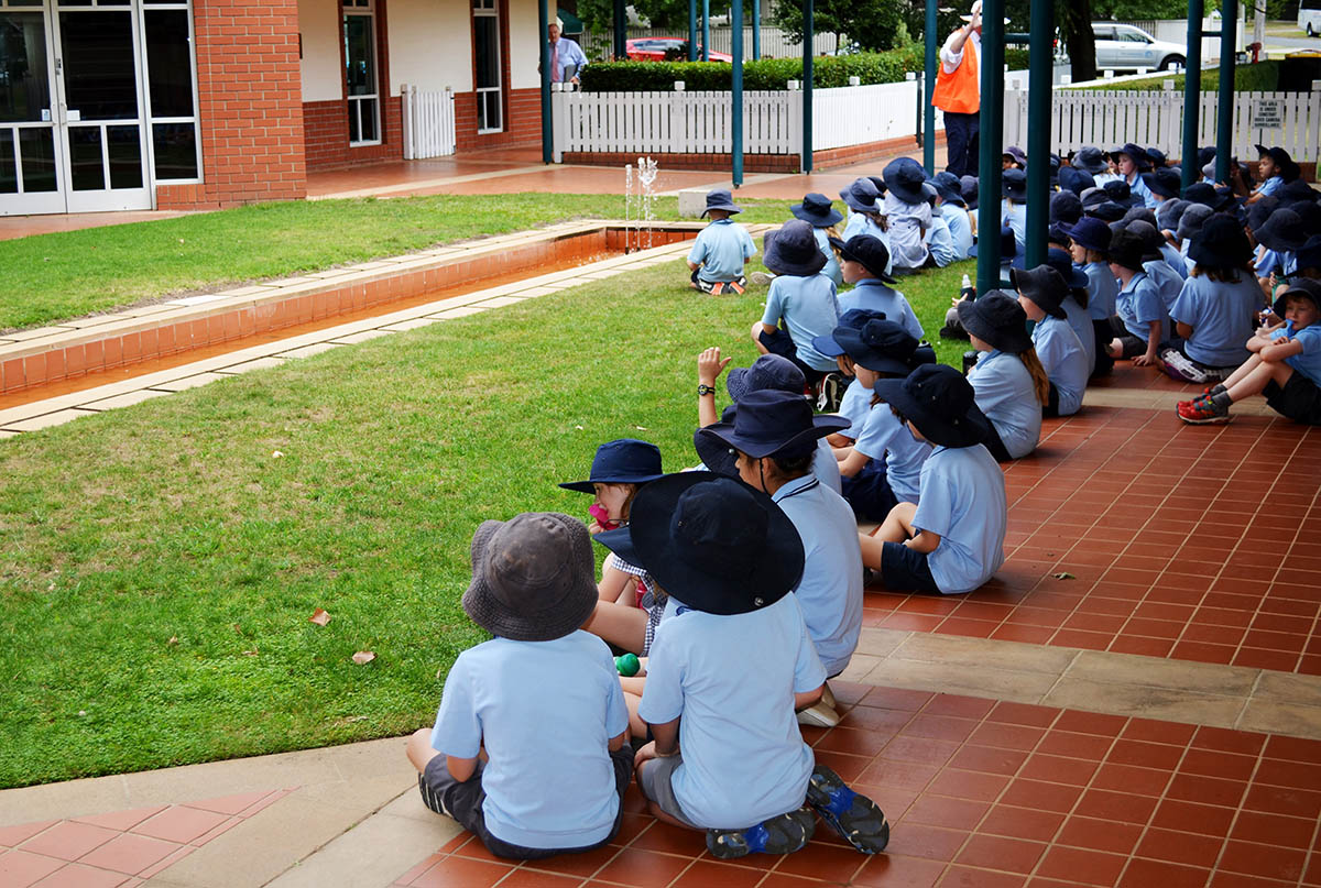 A photo of schoolkids sitting in the shade in summer uniforms