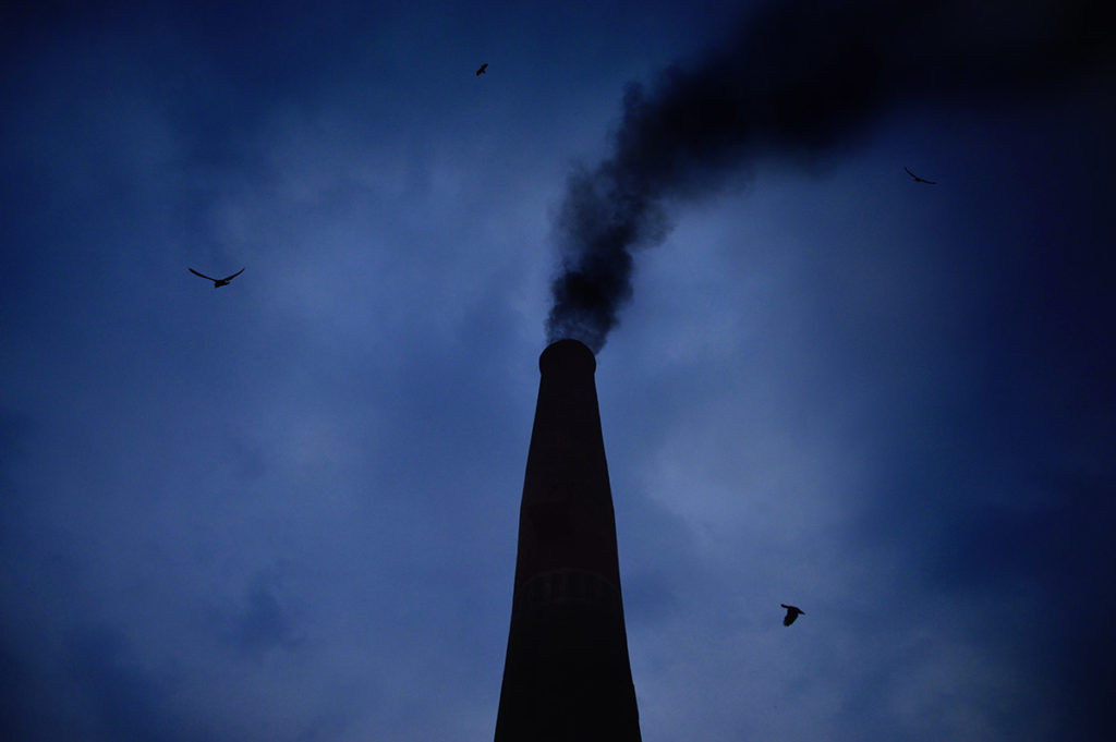 a dark sky behind a smoke stack with a plume of smoke coming out