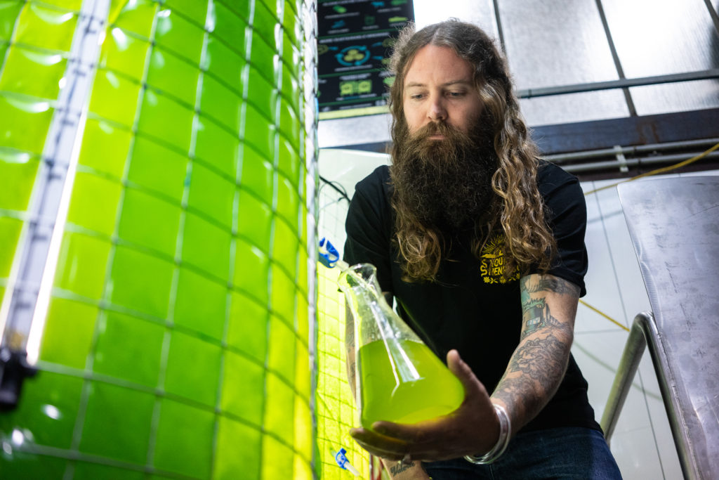 An image of the Young Henrys Co-Founder, Oscar McMahon, with the micro algae bioreactor.