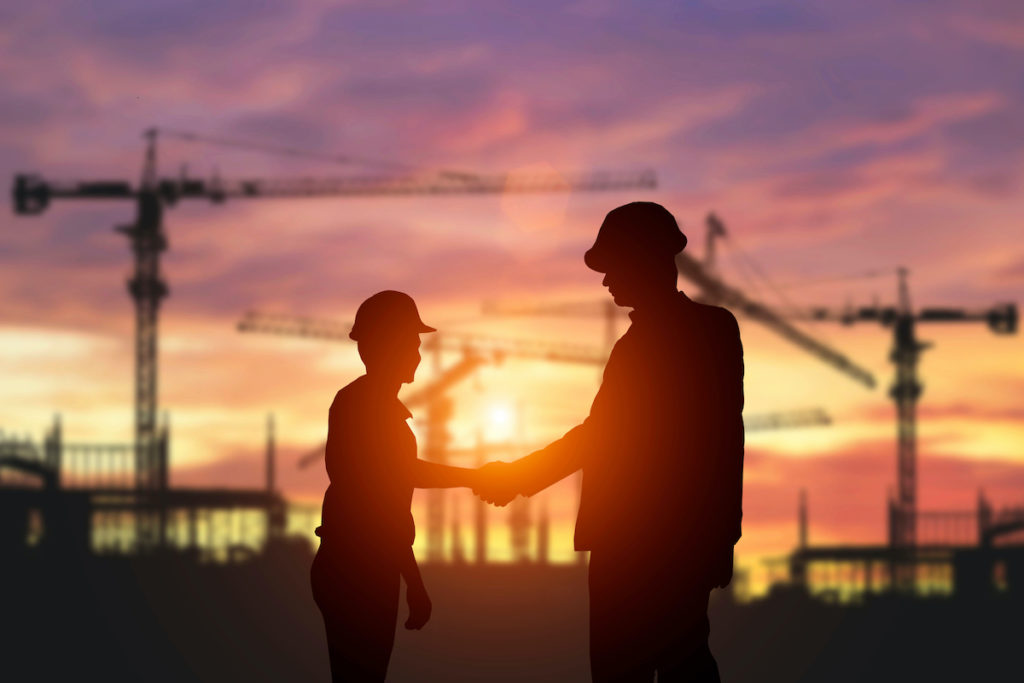 Two workers shake hands backlit by the sun