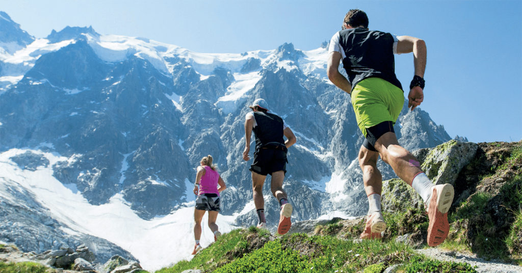 A line of joggers sprinting along a track with the hazy blue summits of glaciers in the distance