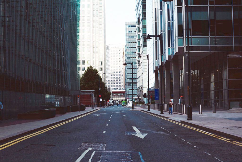 An empty street during covid, except for a single man walking on the footpath carrying groceries.