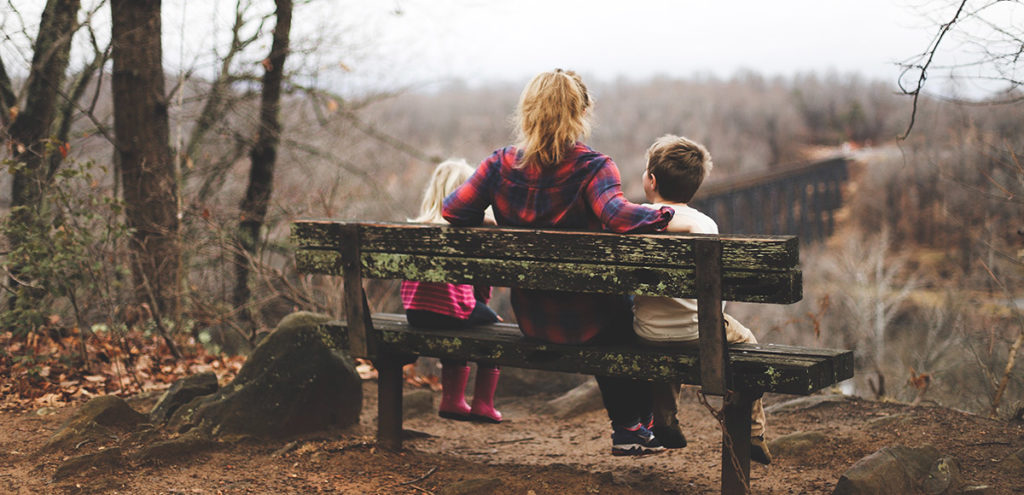 An image of a mum and her two kids sitting on a bench looking out over a valley