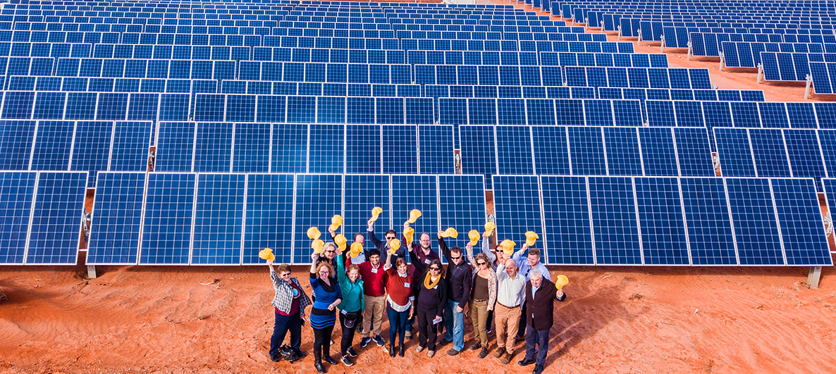 an image of people smiling in front of solar panels with their hats in the air (Photo credit: Andrew Correll)