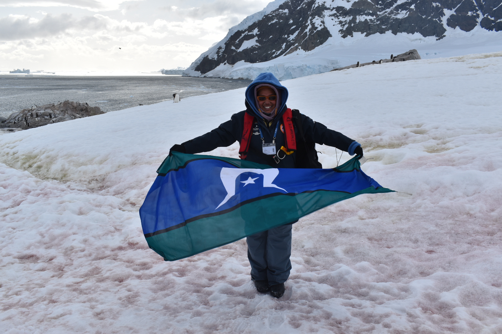 An Image of Tishiko King in Antarctica holding a Torres Strait Islands flag.