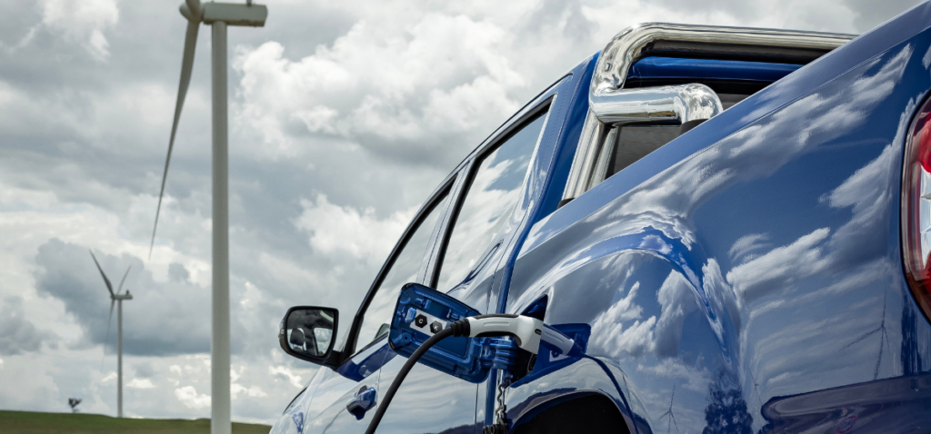 Electric Ute charging in front of wind turbines