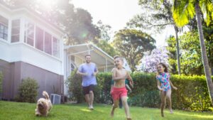 An image of a happy family running through the sprinklers on a sunny day.